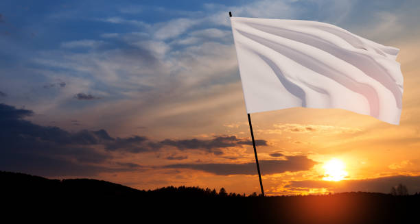 White flag waving in the wind on flagpole against the sunset sky with clouds. stock photo