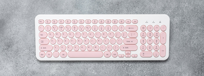 White keyboard with pink keys on a gray concrete background. Top view, flat lay, banner.