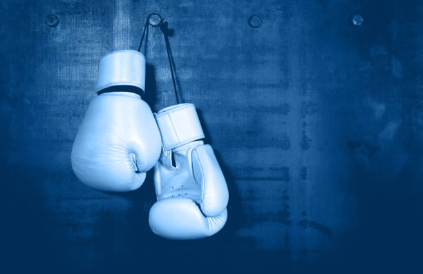 White leather boxing gloves hanging on blue wall Close up pair of clasic white leather boxing gloves hanging over dark blue wall with copy space boxing glove stock pictures, royalty-free photos & images