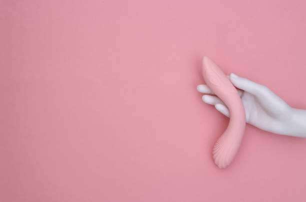 White mannequin hand holding female sex toy on pink pastel background. Top view. Minimalism stock photo