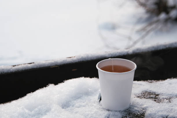 White paper cup with hot tea on snowy table. stock photo