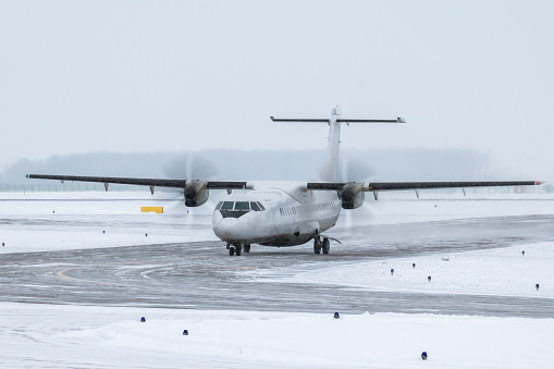 White passenger turboprop aircraft taxiing on the taxiway in a severe blizzard