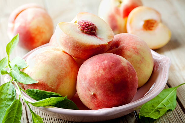 White peaches in a bowl with green leaves stock photo