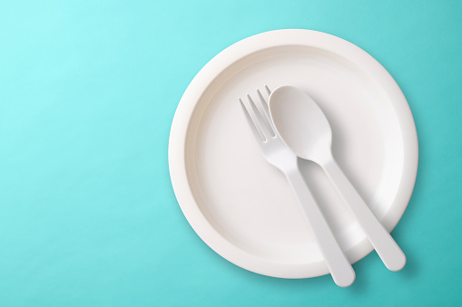 Overhead shot of white plastic plate, Folk, and spoon on blue background.