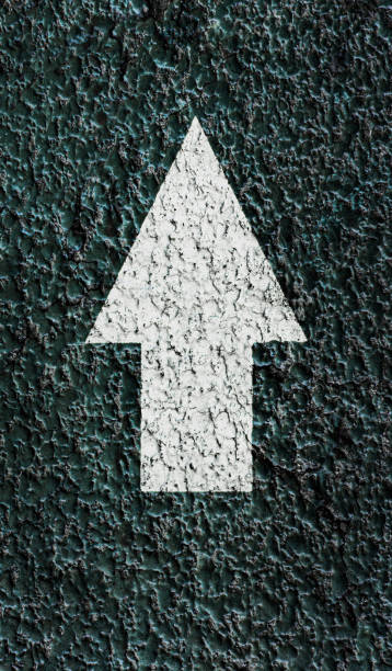 White pointing arrow on a textured asphalt surface. Direction icon. stock photo