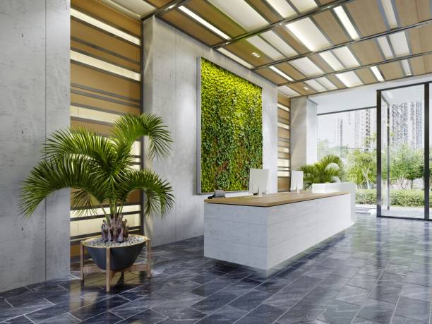 White reception desk in an office building with a green wall and illuminated wood paneling and flowerpots. stock photo