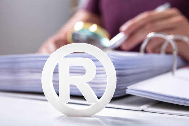 White Registered Trademark Sign Near Documents Close-up Of White Registered Trademark Sign Near Documents Over Desk intellectual property stock pictures, royalty-free photos & images