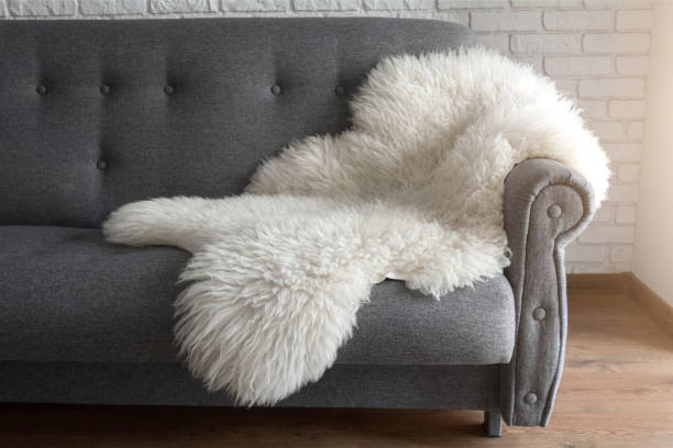White sheep skin on a gray sofa. A cozy place to relax in the apartment. Modern Scandinavian style interior stock photo