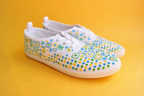white sneakers with hand-painted geometric shapes on a yellow background stock photo