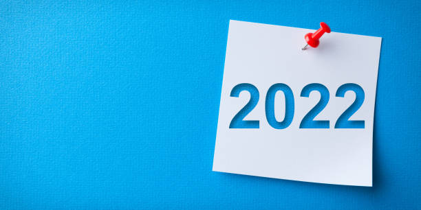 White Sticky Note With Happy New Year 2022 And Red Push Pin On Blue Background stock photo