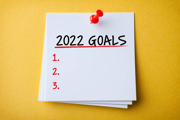 White Sticky Note With New Year 2022 Goals And Red Push Pin On Yellow Background stock photo