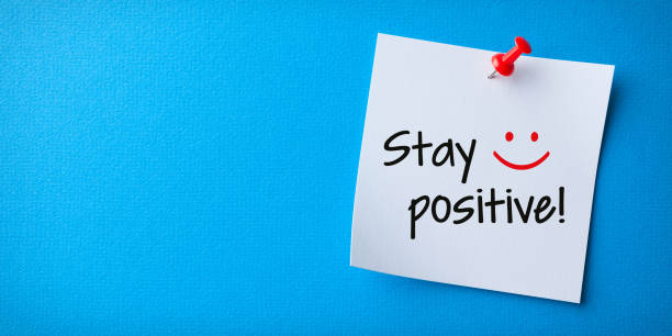 White Sticky Note With Stay Positive And Red Push Pin On Blue Background stock photo