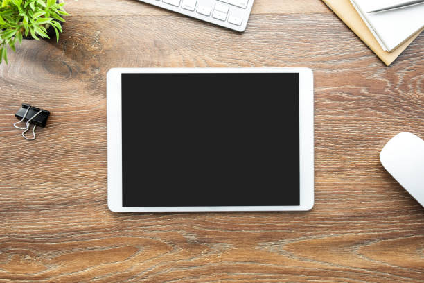 White tablet with black blank screen is on top of wood desk table with supplies. Top view, flat lay. White tablet with black blank screen is on top of wood desk table with supplies. Top view, flat lay. digital tablet photos stock pictures, royalty-free photos & images