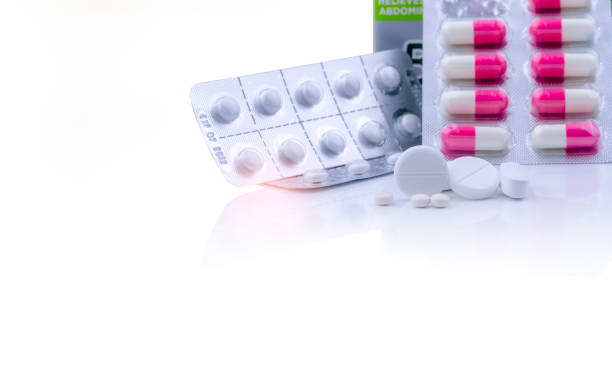 White tablets pills on white table and blurred pink-white capsule pills in blister pack. Pharmaceutical products. Pharmaceutical industry. Round and oval tablets pills. Healthcare and pharmacy. White tablets pills on white table and blurred pink-white capsule pills in blister pack. Pharmaceutical products. Pharmaceutical industry. Round and oval tablets pills. Healthcare and pharmacy. pics for amoxicillin stock pictures, royalty-free photos & images
