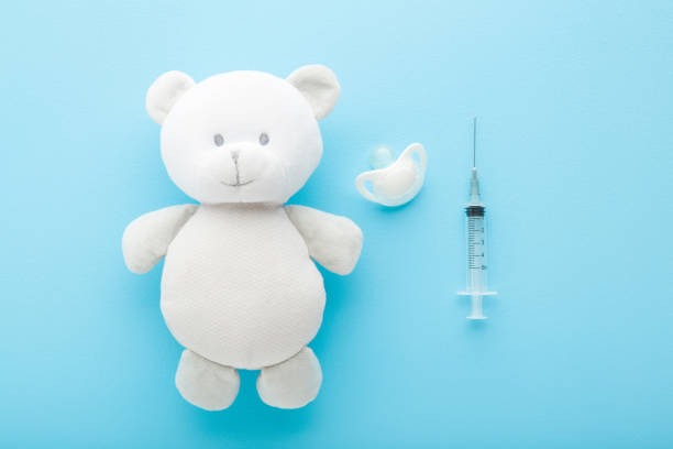 White teddy bear, soother and syringe on light blue table background. Pastel color. Closeup. Babies vaccination and healthcare concept. Top down view. stock photo