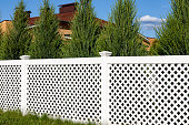 istock White vinyl fence in a cottage village. Tall Thuja bushes behind the fence. 1302489737