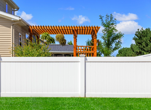 A modern middle class home with its backyard being enclosed for privacy by a new, modern style white vinyl fence. Green grass, and blue sky is in the background.