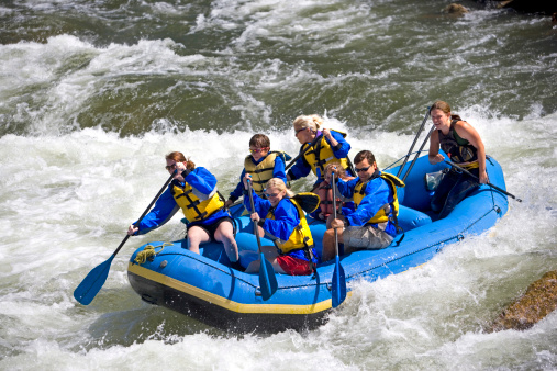 A group of men, women and children, with a guide, white water rafting on the Arkansas River in Colorado.