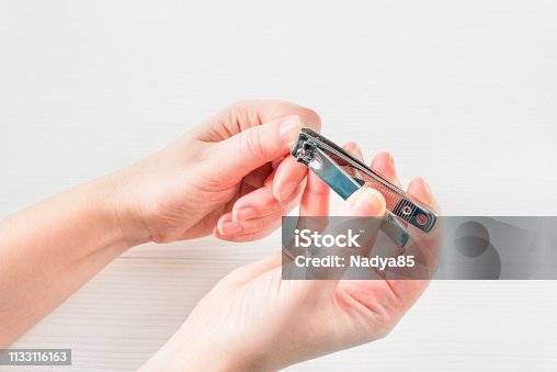 istock White Woman's Hand With Healthy Natural Nails Getting Nail Care Procedure. White female hands cutting nails with nail cutter on white wooden background. Beauty Manicure. Personal Hygiene. 1133116163