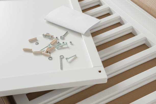 White wooden planks, screws and instruction book for crib in cardboard box. Preparation for future baby. Assembling new furniture. Closeup. stock photo