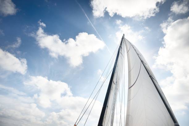 White yacht sails against clear blue sky with lots of clouds. Sailing in an open Mediterranean sea. Idyllic cloudscape. Summer vacations, leisure activity, sport and recreation, private wessel stock photo
