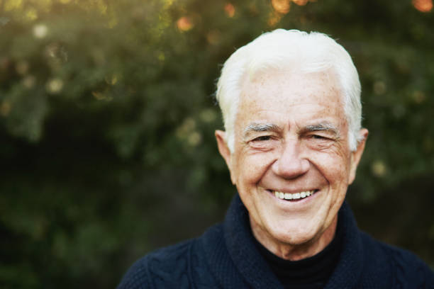 White-haired old man smiles happily outdoors in a garden stock photo