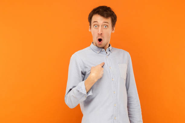 Who, i'm? Shocked man looking at camera and pointing finger himself Who, i'm? Shocked man looking at camera and pointing finger himself. Studio shot, orange background one man only stock pictures, royalty-free photos & images