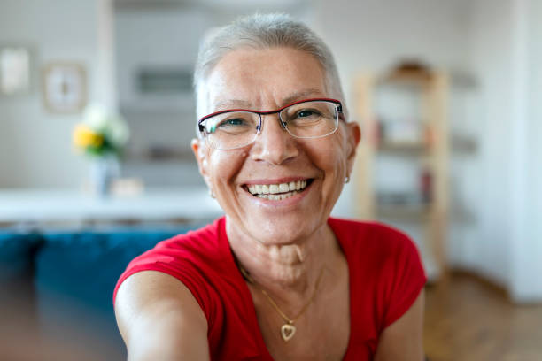 Who said selfies are just for the youth? Technology, Communication and People Concept - Happy Smiling Senior Woman With Eyeglasses Taking Selfie at Home. Close Up Portrait of Elderly Woman in the Livingroom 65 69 years stock pictures, royalty-free photos & images