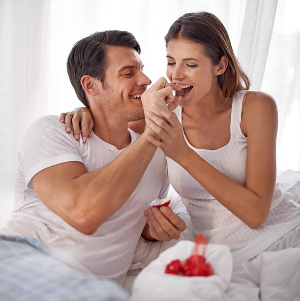 Who says chocolate isn't a  good breakfast?! Shot of an affectionate young husband feeding his wife chocolate couple eating chocolate stock pictures, royalty-free photos & images