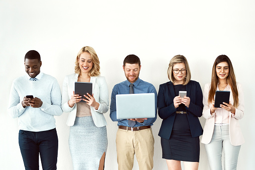 Shot of a group of work colleagues standing next to each other while using electronic devices against a white background