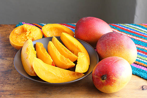 Whole and Sliced Mangos on Table stock photo