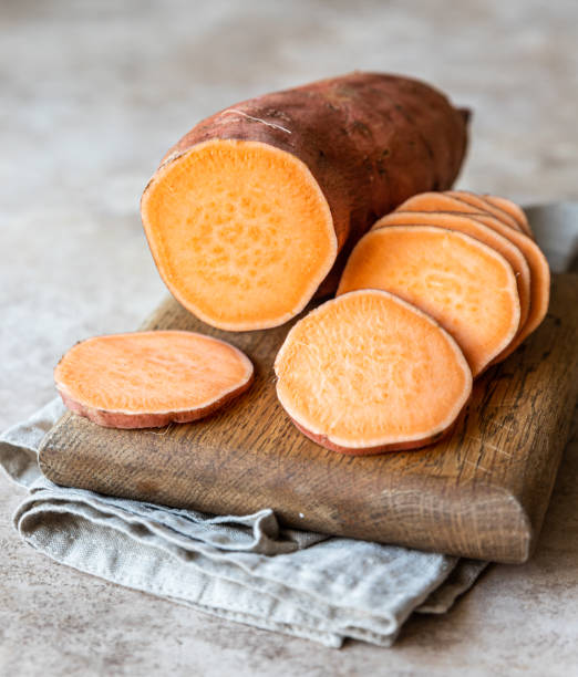 Whole and slices raw sweet potatoes on wooden kitchen board, organic yam. The farm food. stock photo