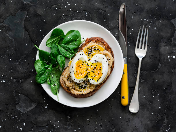 Whole grain bread hummus, boiled egg, sesame sandwich and fresh spinach on a dark background, top view stock photo