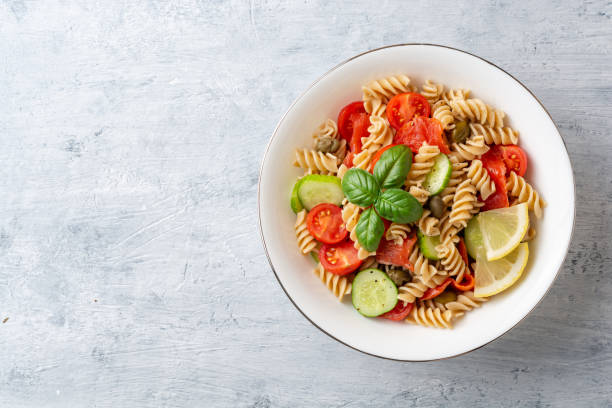 Whole wheat pasta salad with cucumbers, cherry tomatoes, salted salmon and capers on concrete background stock photo