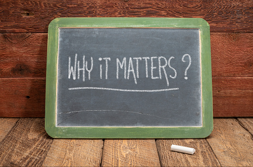 Why it matters? White chalk handwriting on a vintage slate blackboard against rustic wood, business and education concept
