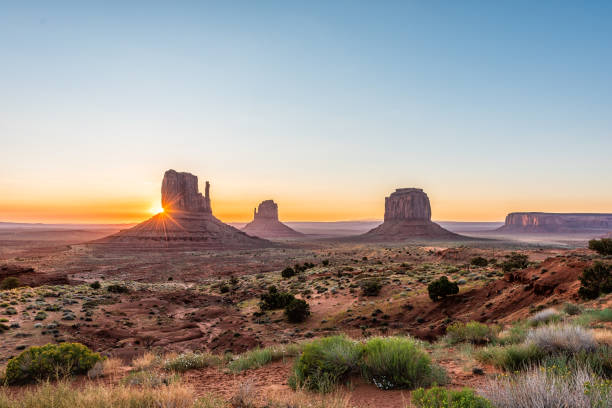 Wide angle overlook panoramic view of buttes and horizon in Monument Valley at sunrise colorful light and sunburst in Arizona with orange rocks stock photo