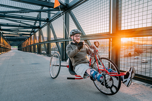 Handsome Young Man with Myelomeningocele Spina Bifida Riding a Red Handcycle Wearing Orthotic Leg Braces for Adaptive Exercise Outdoors in the Spring. Overcoming the Stigma and Challenges of Disability can be Fun on a Hand bike!