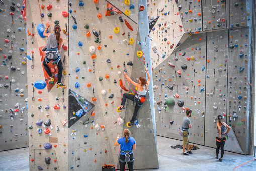Caucasian men and women in teens and 20s working together in practice sessions moving up vertical walls in sport climbing gym.