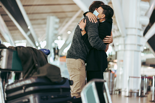 Husband and wife meeting after long separation during covid-19 outbreak at airport arrival gate. Female with face mask welcoming male traveler at airport arrival.