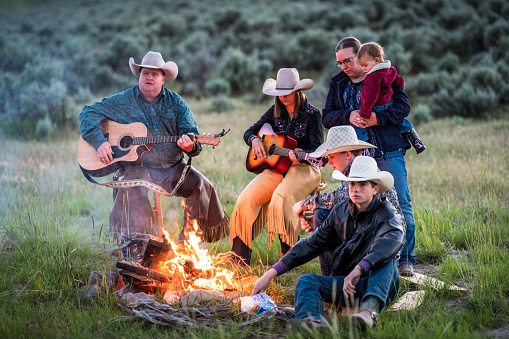 A group of ranchers playing music and singing together at dusk in the country.