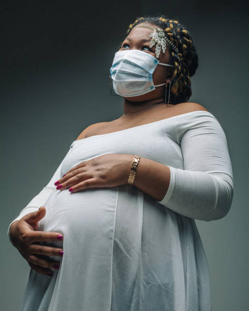 I will always be there for you! Wearing a protective mask, a beautiful pregnant young woman, dressed in white, keeping her hands on her stomach in a protective way. Real people photography. beautiful haitian women stock pictures, royalty-free photos & images
