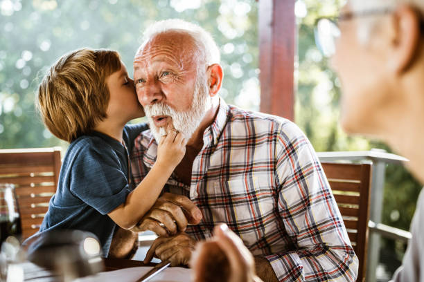 I will whisper you something granddad! Surprised senior man listening a secret that his grandson is whispering to him during a meal on a terrace. whispering stock pictures, royalty-free photos & images