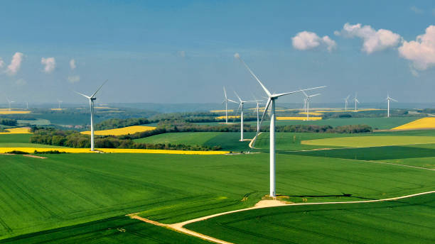 Wind farm in France French landscape with a wind farm above rapeseed fields and forests under an azure blue sky dotted with a few small white clouds. vertical axis wind turbine stock pictures, royalty-free photos & images