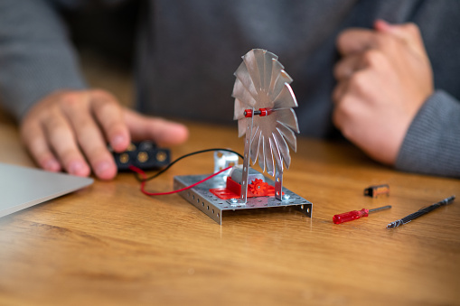 A schoolboy is testing his wind turbine model for his science project, made of metal and plastic, working on electricity.
