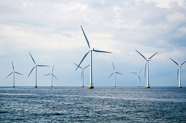 Wind turbines at sea Nine wind turbines at sea. Windmills in blue ocean with a clouded blue sky. wind turbine stock pictures, royalty-free photos & images