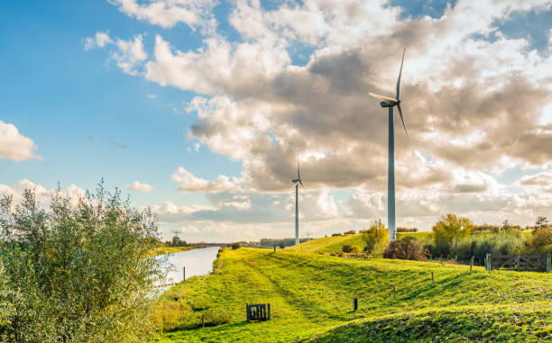 Photo of Wind turbines in a Dutch landscape with dikes and threatening clouds in a blue sky