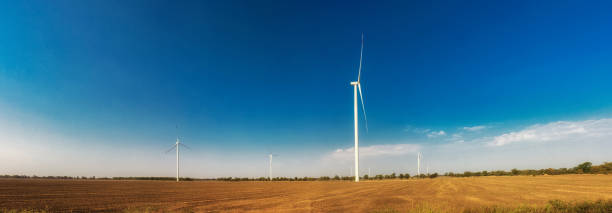 Wind turbines on field. Empty field in foreground, blue sky  on background. Alternative energy source, production and power generation. Ecology and freedom concept. Panorama. stock photo