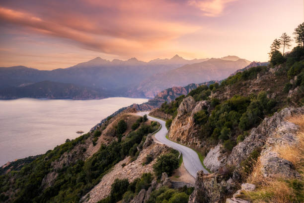 winding coast road in Corsica The D824 road winding its way along the coast from Capu Rossu towards Piana on the west coast of Corsica as the early  morning sun lights up the distant mountains corsica stock pictures, royalty-free photos & images