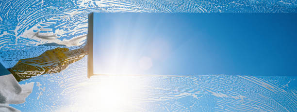 Window cleaner cleaning window with squeegee and wiper on a sunny day with a bright blue sky stock photo