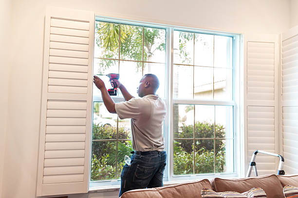 Window treatment installer installs wooden shutters  RM stock photo